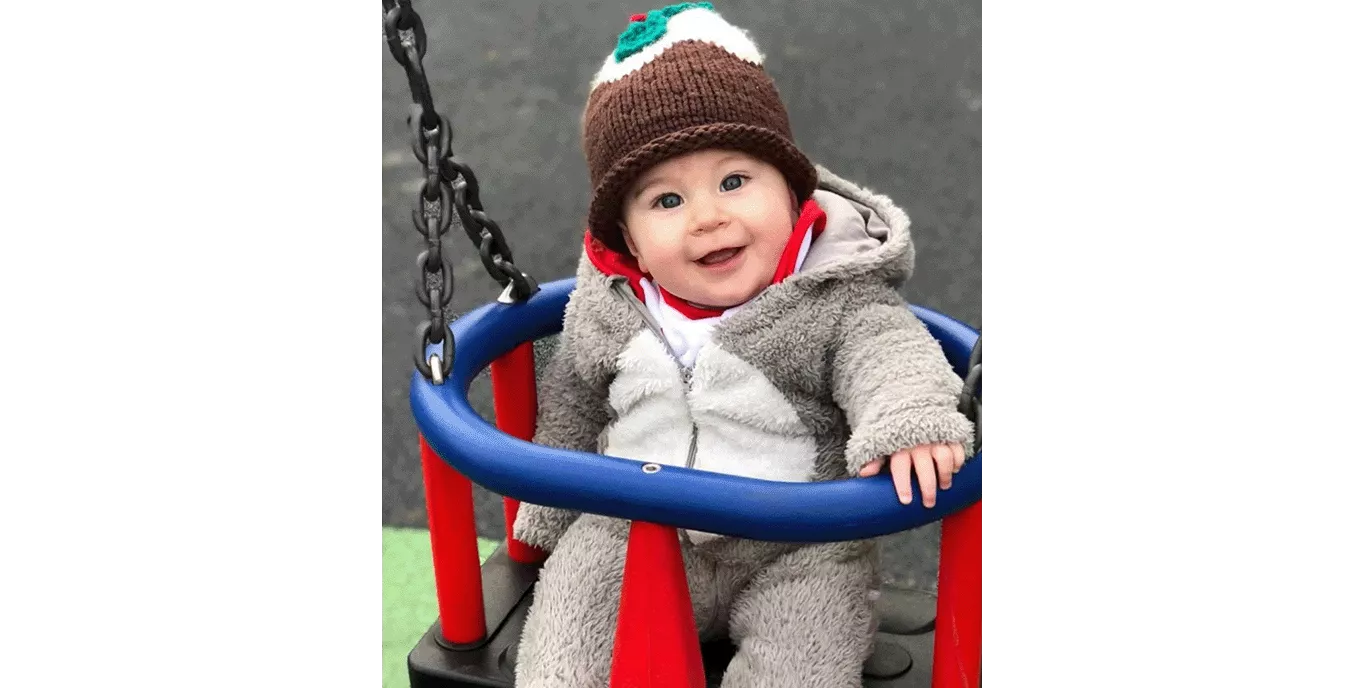 Baby in a swing wearing a Christmas pudding hat