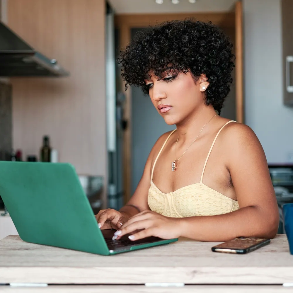 Woman sitting at her kitchen counter looking at her laptop