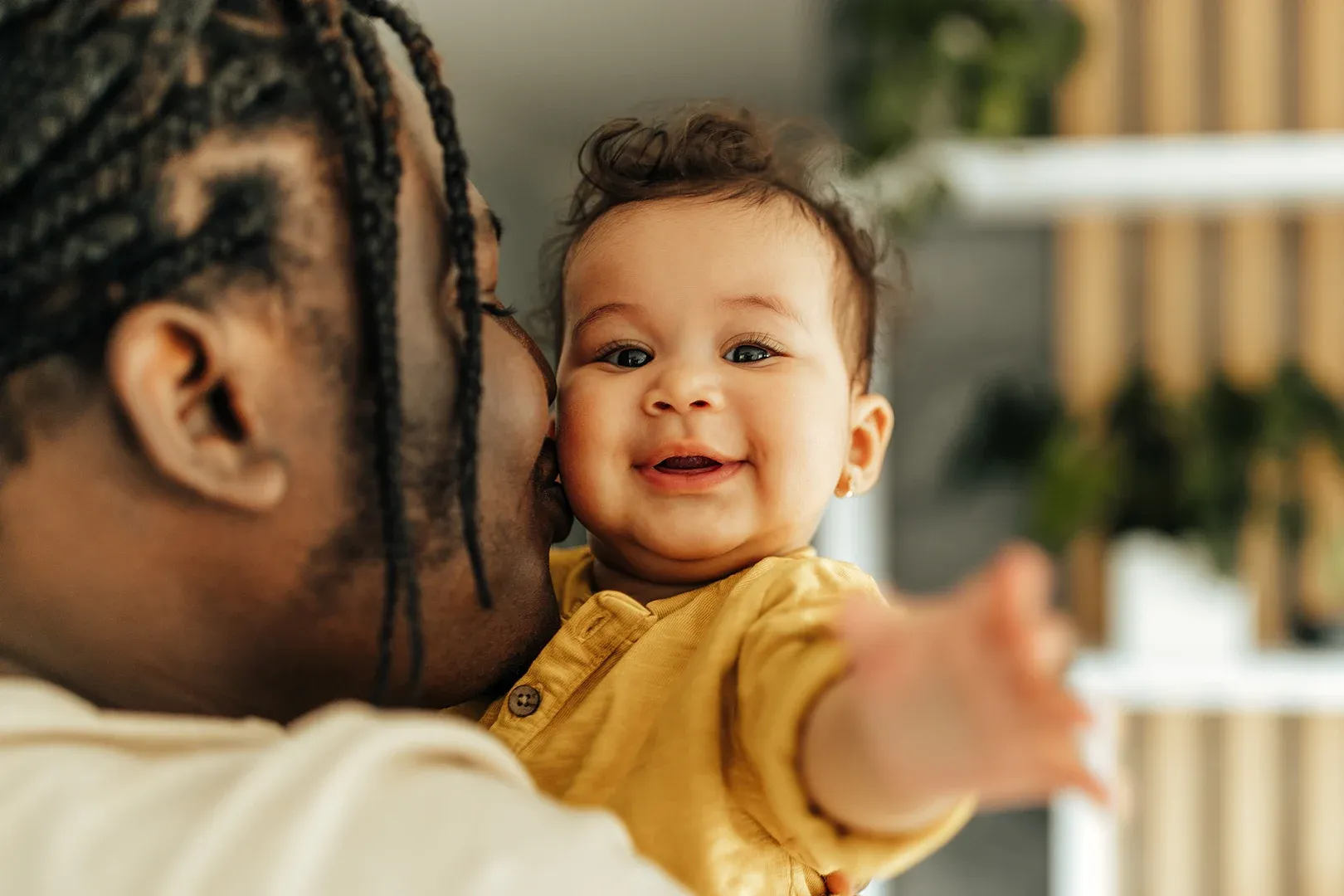 smiling baby held in fathers arms reaches out toward the camera