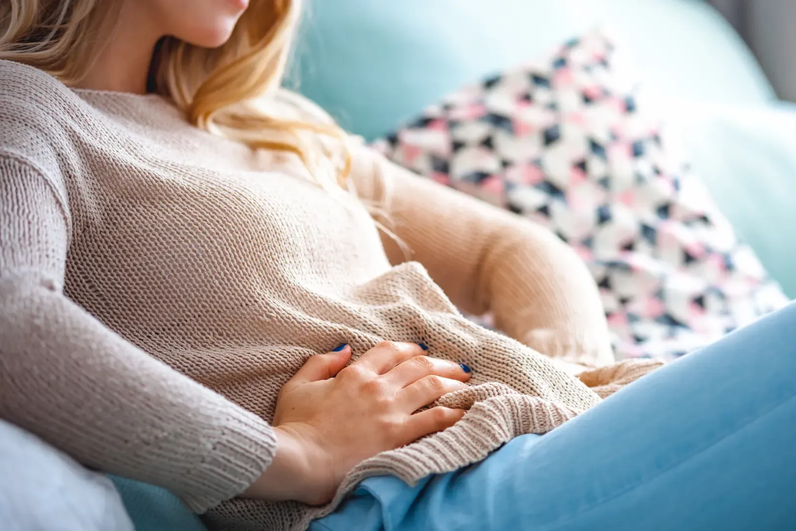 woman sitting on sofa holding her stomach in pain