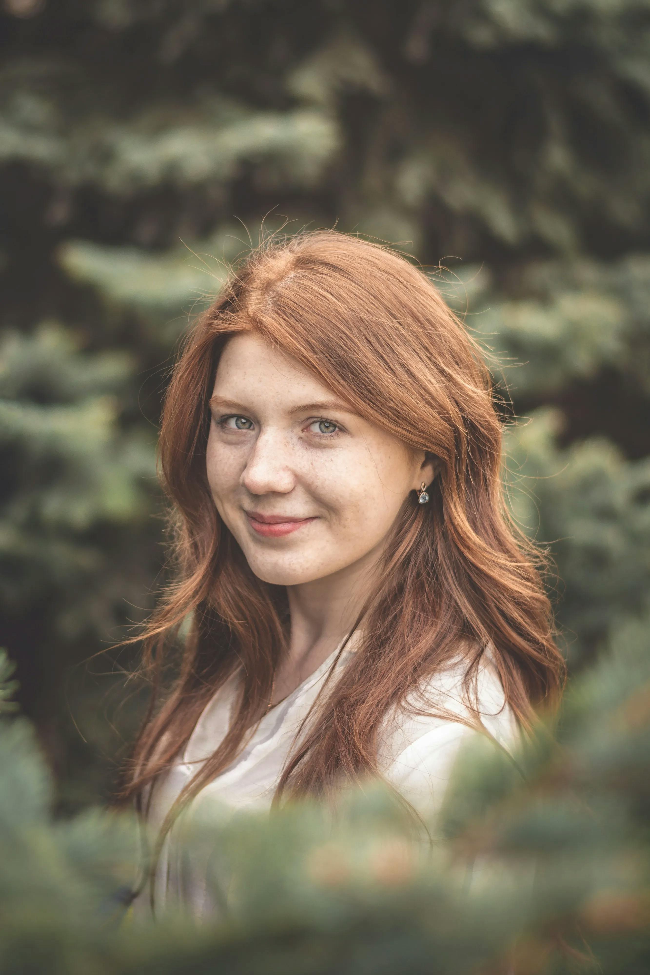 Redheaded woman smiling outside amongst greenery