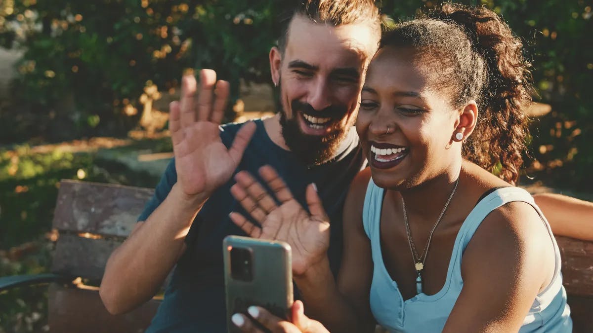 A young couple smiling and waving at someone through their phone