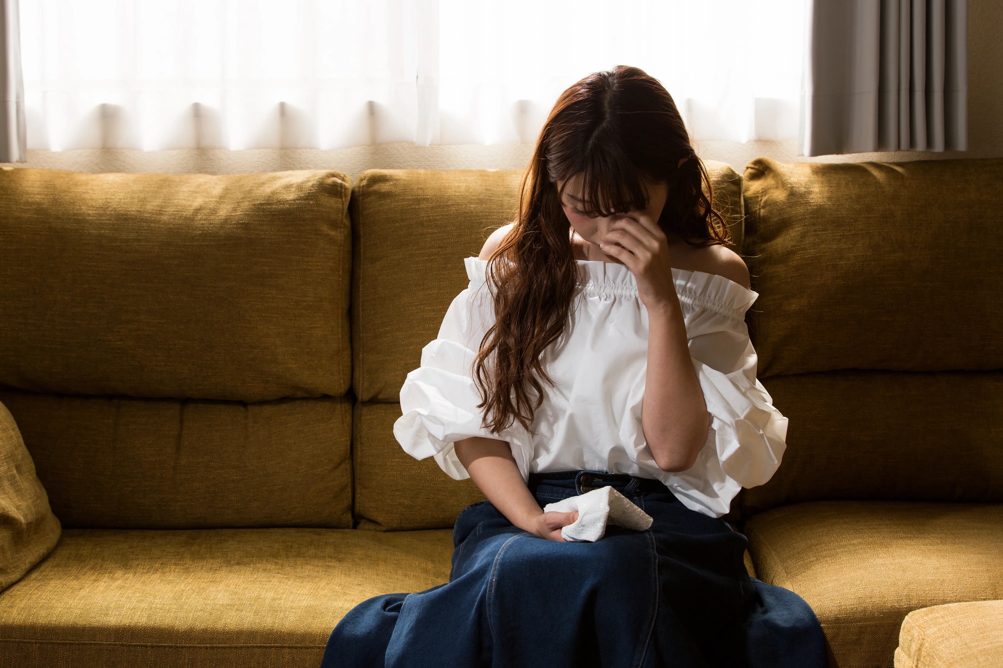 A woman sat on a sofa crying with a tissue in her hand