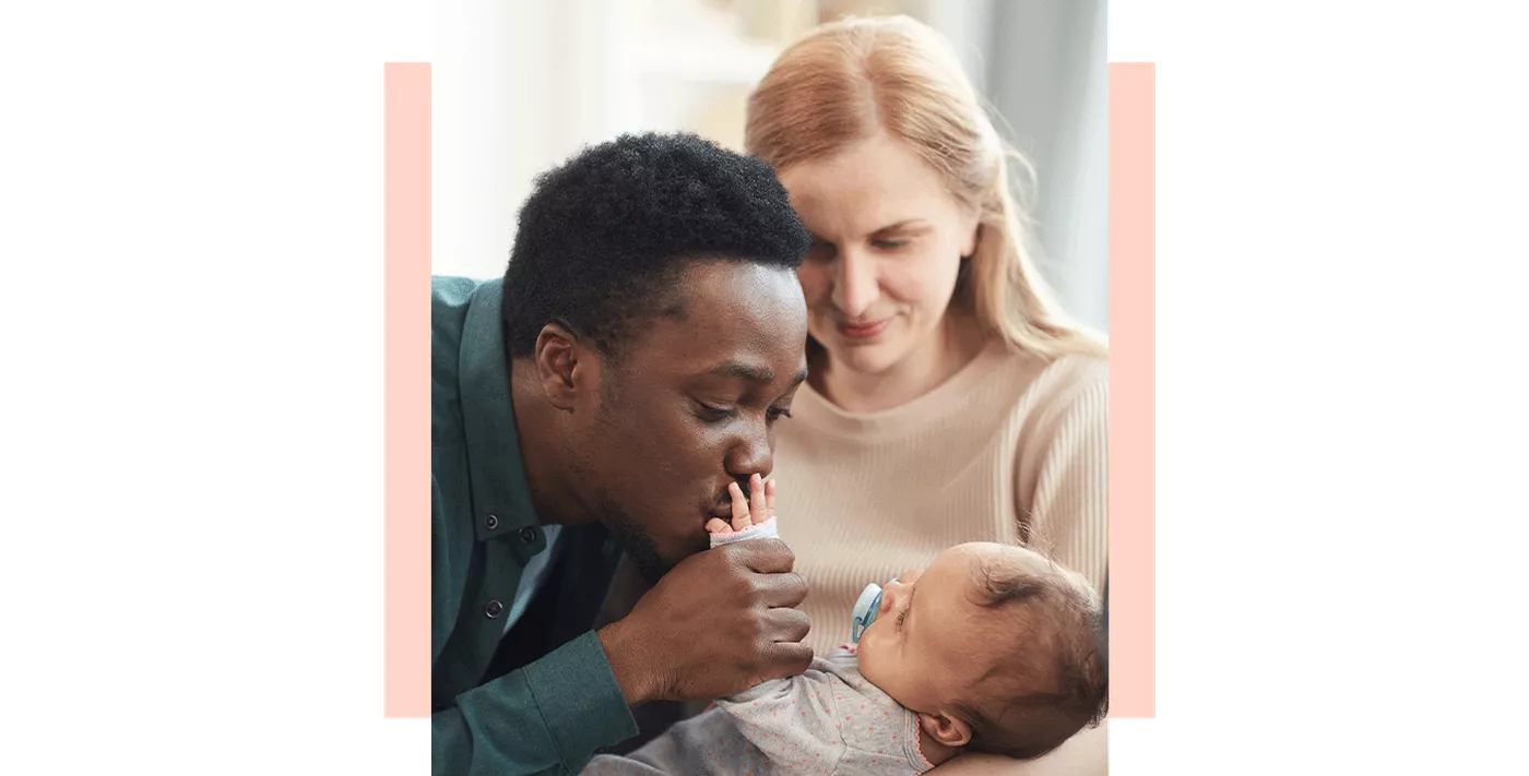 Woman holding her baby while father kisses the childs hand
