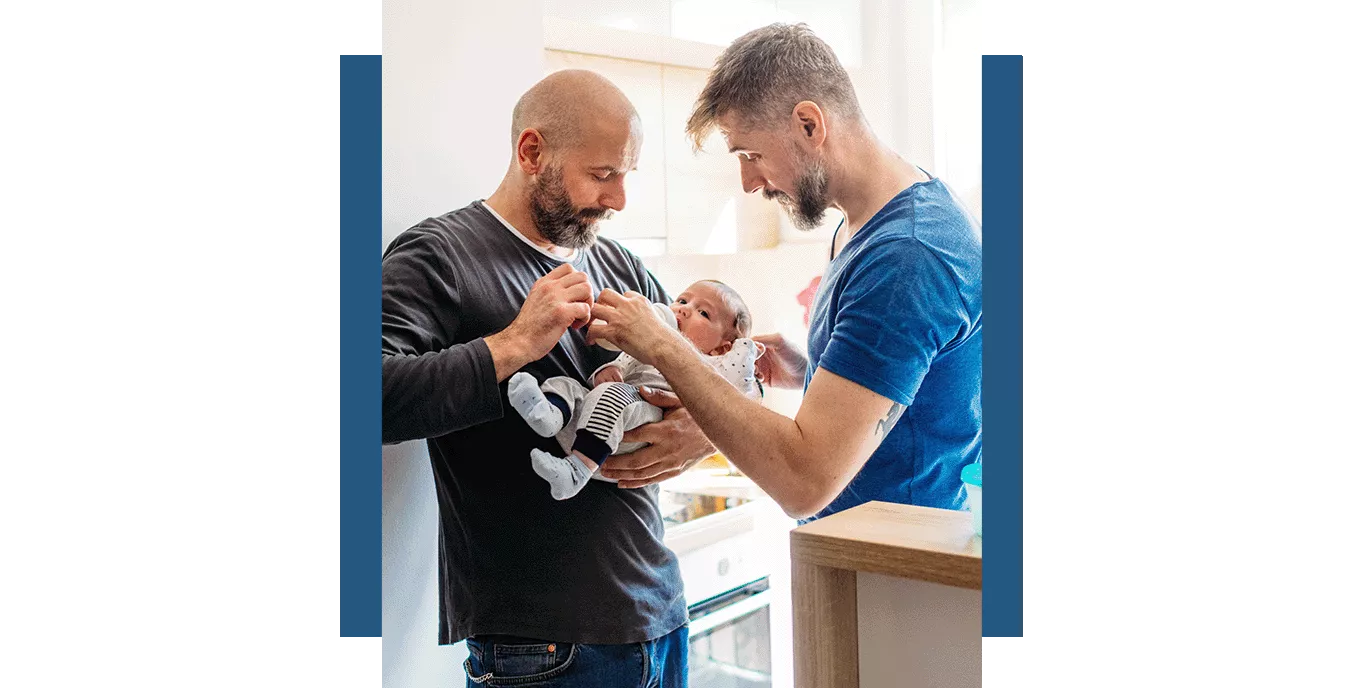 Two dads hold and feed their baby together