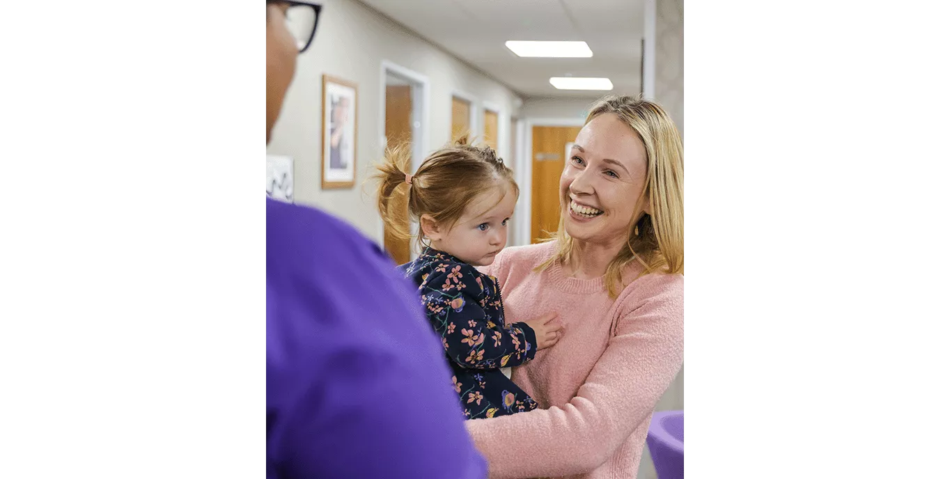 Woman laughing and holding her daughter while talking to a nurse