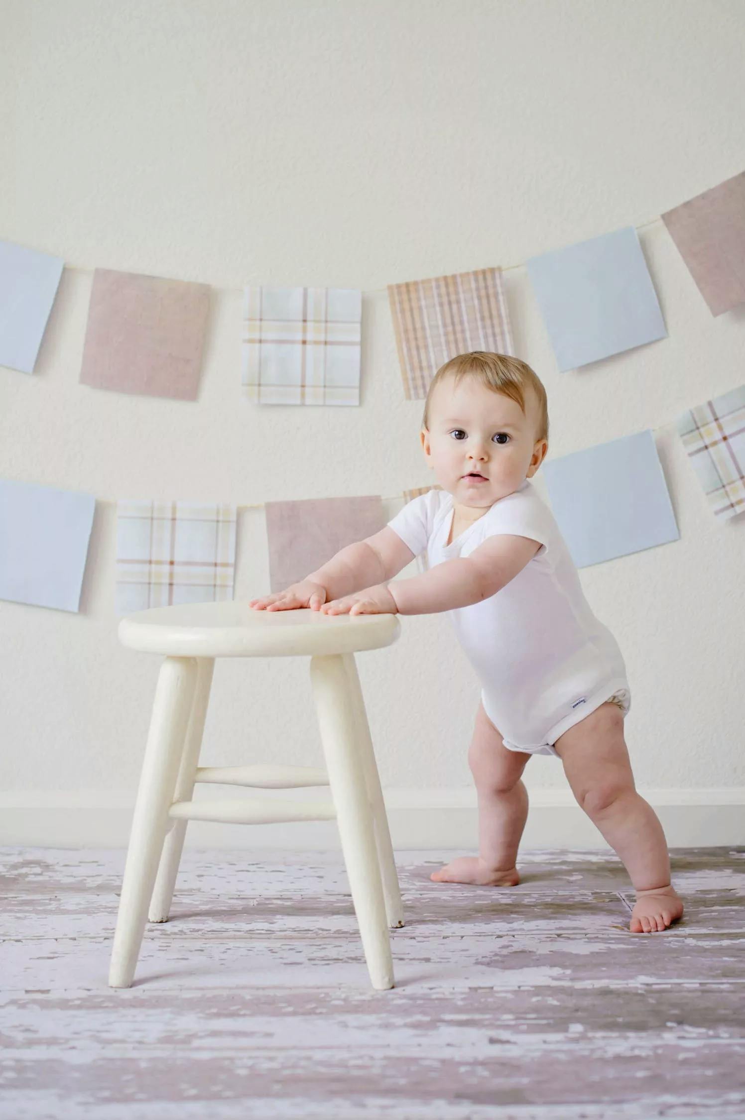 baby standing up beside a stool